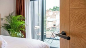 Hotelkamer met een bed, een potplant en uitzicht door een glazen deur op een buitenruimte met een tafel en stoelen.