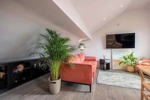 A modern living room with a sofa, a large potted plant, a flat-screen TV, and a dining area. - The Carillon Suite - Stylish Duplex w/ York Minster Views & Free Parking (York)