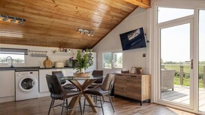 Een keuken met een houten plafond, een wasmachine, een eettafel met stoelen en een groot raam.