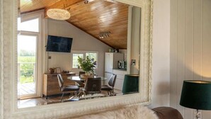 Een knus vertrek met een houten plafond, een eethoek met stoelen en een tafel, en een uitzicht door een raam.