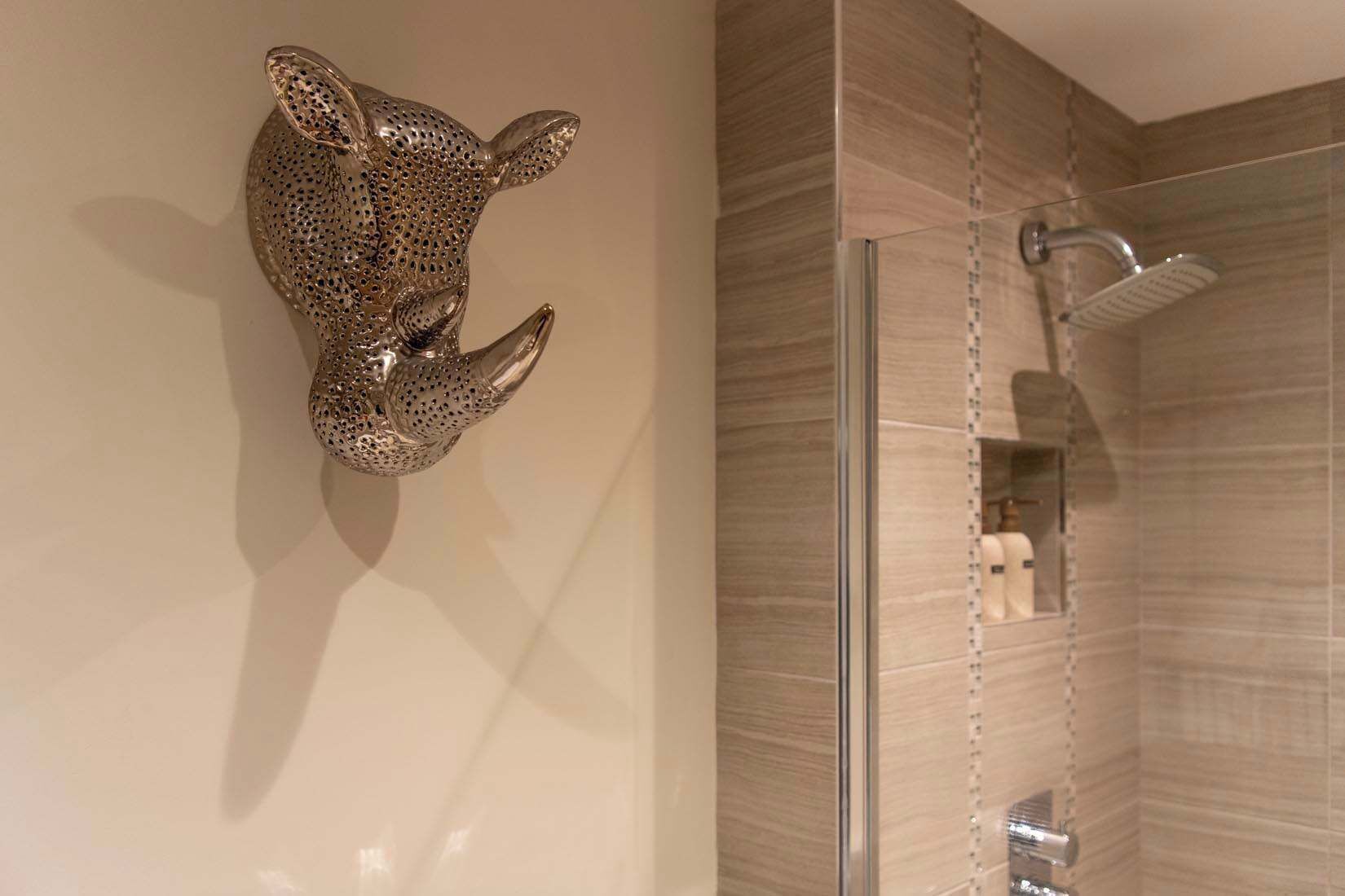 A bathroom with a glass shower enclosure, a wall-mounted towel rack, and a decorative metal sculpture.