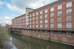 A large brick building with multiple windows, a waterway in front, and a bridge. - The Foss Suite - Luxury River View Studio in Central York (York)