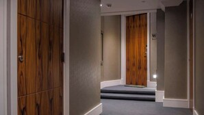 Un couloir avec des portes en bois, un sol recouvert de moquette et une porte en bois au bout.