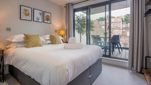 A hotel room with a large bed, a balcony with chairs, and framed artwork on the wall. - The Botanical Suite - Luxury Apartment with Balcony & York Minster View (York)