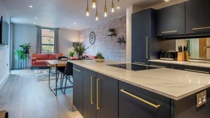 A modern kitchen with dark cabinetry, a marble countertop, and pendant lighting. - The Botanical Suite - Luxury Apartment with Balcony & York Minster View (York)