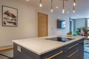 A modern kitchen with a marble countertop, built-in oven, and pendant lighting. - The Botanical Suite - Luxury Apartment with Balcony & York Minster View (York)