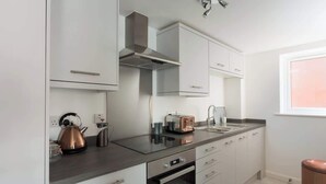 A modern kitchen with white cabinets, a stainless steel range hood, a built-in oven, and a window with a view. - The Aura Suite - Stylish Apartment Near York Minster Free Parking (Layerthorpe)