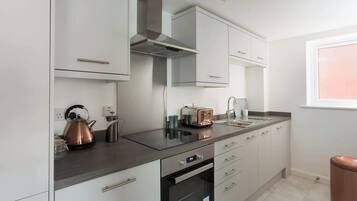 A modern kitchen with white cabinets, a stainless steel range hood, a built-in oven, and a window with a view.