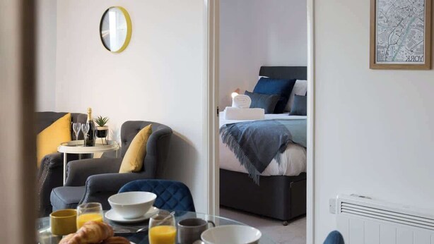 A hotel room with a dining area, a bed with a headboard, a radiator, and a framed map on the wall. - The Aura Suite - Stylish Apartment Near York Minster Free Parking (Layerthorpe)