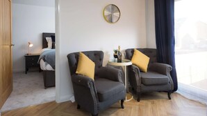 A room with two armchairs, a small round table with a bottle, a clock on the wall, and a view through a window. - The Aura Suite - Stylish Apartment Near York Minster Free Parking (Layerthorpe)