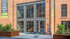 A brick building with large glass windows and a door, a sign advertising loft-style apartments, and a contact number. - The Palm Suite - Luxury Loft Apartment w/ Private Balcony & City Views (York)