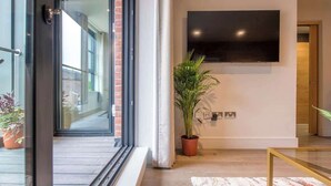 A modern interior with a large flat-screen TV mounted on the wall, a potted plant, and a glass door leading outside. - The Palm Suite - Luxury Loft Apartment w/ Private Balcony & City Views (York)