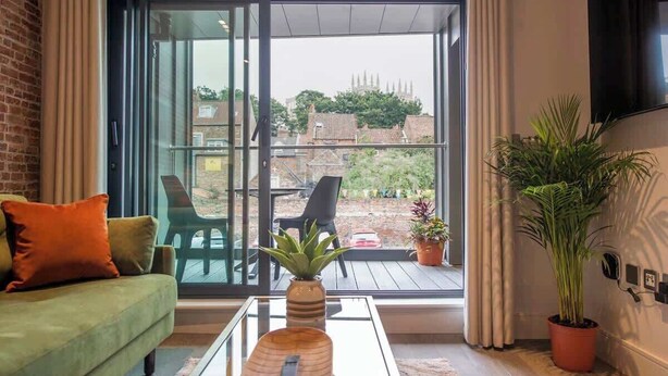 A modern living room with a green sofa, a glass coffee table, and a sliding glass door leading to an outdoor patio. - The Palm Suite - Luxury Loft Apartment w/ Private Balcony & City Views (York)