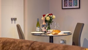 A dining table with a bottle of wine, glasses, a plate of food, and a vase of flowers. - The Refinery Suite - Stylish York Apartment in Historic Building (York)