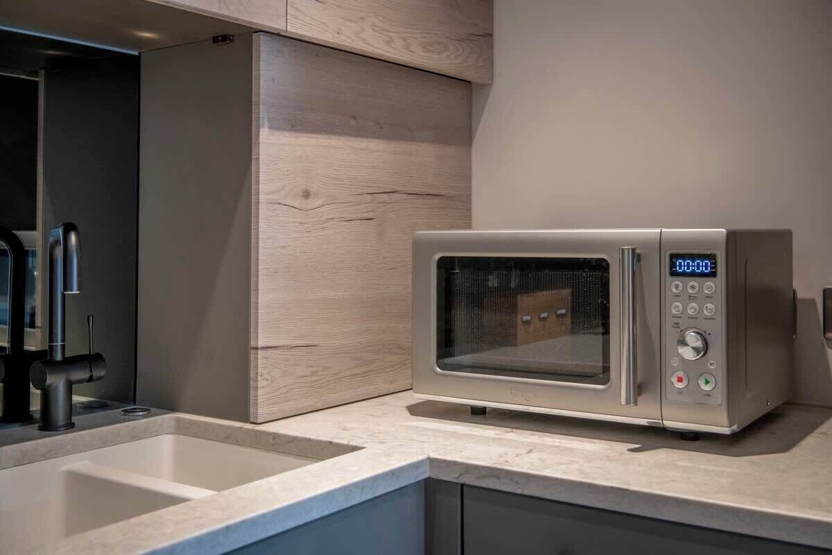 A modern kitchen with a built-in microwave, a sink, and a wooden cabinet.