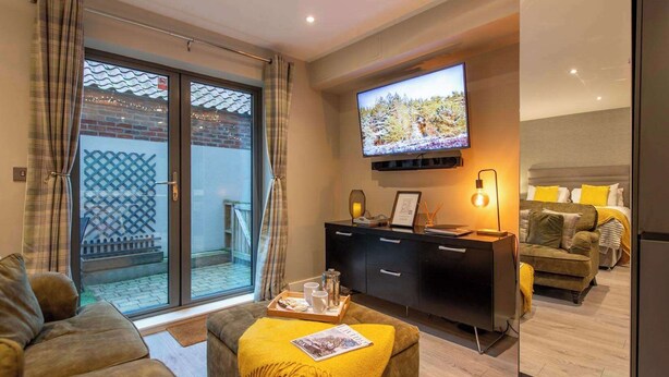 Un salon moderne avec un canapé, une table basse sur laquelle repose un magazine, un téléviseur fixé au mur et un balcon offrant une vue agréable.
