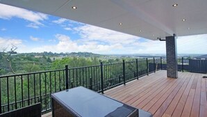 A covered outdoor area with a table and chairs, a view of greenery, and a railing. - Your Private Escape with city views (Totara Park)