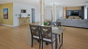 A modern living room with a dining area, a grey sofa, and a TV mounted on the wall. - Your Private Escape with city views (Totara Park)