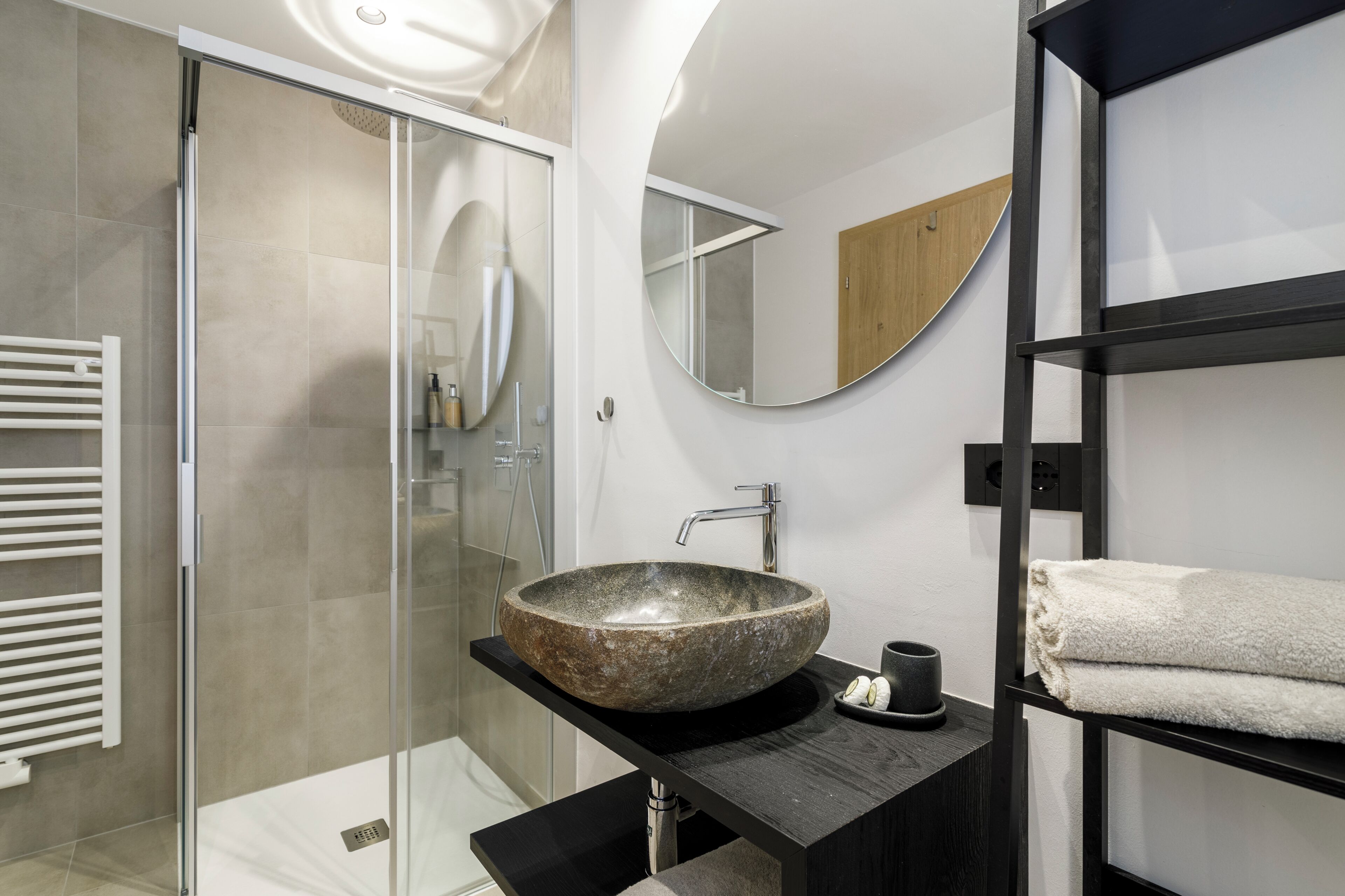 Un baño moderno con un lavabo de piedra, una cabina de ducha de vidrio y un mueble de tocador negro.