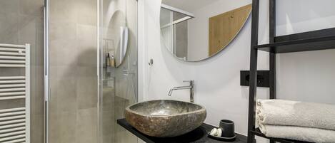 Un baño moderno con un lavabo de piedra, una cabina de ducha de vidrio y un mueble de tocador negro.