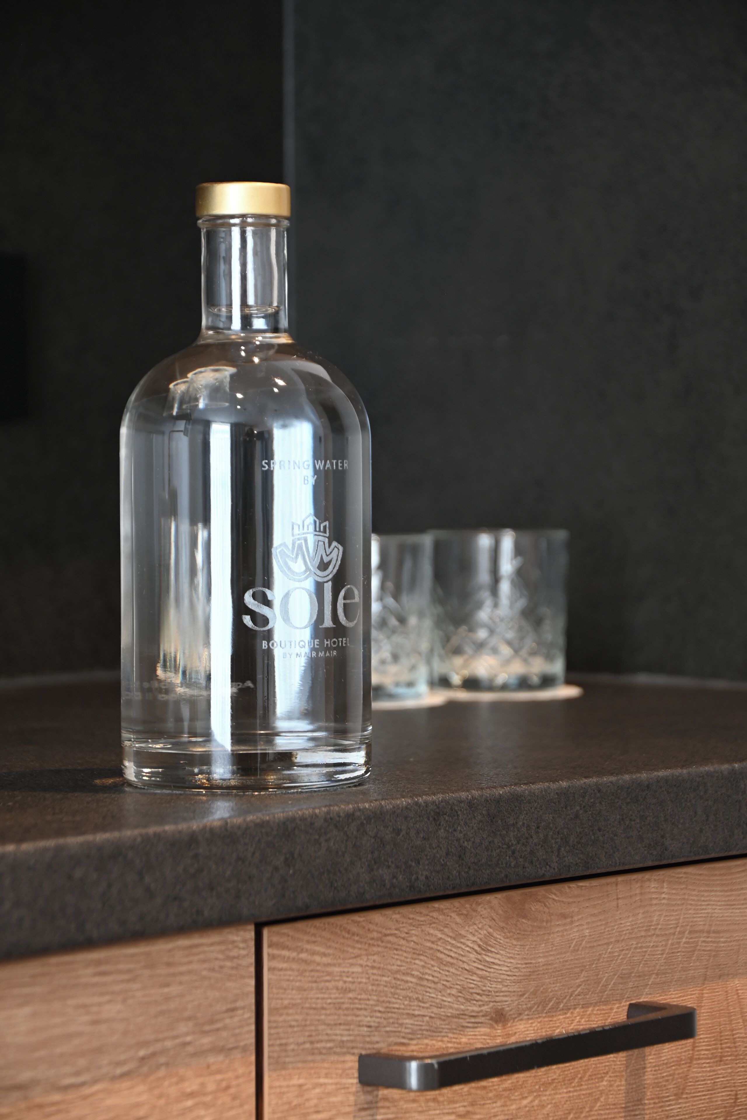 A clear bottle of Spring Water on a dark countertop with a wooden drawer below.