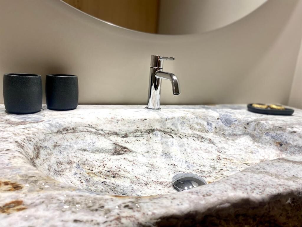 Un baño con un lavamanos de mármol, un grifo cromado y dos tazas negras.