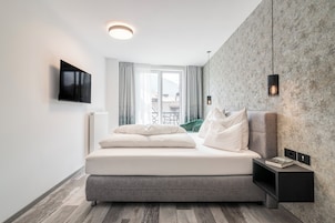 A modern bedroom with a bed, a mounted TV, a bedside table with a book, and a view of the outdoors.