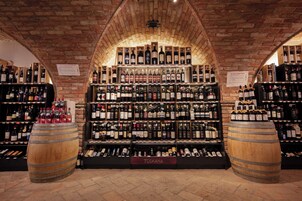 A wine cellar with wooden barrels and shelves of wine bottles.