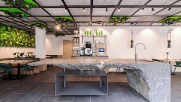 Un interior moderno con una isla grande de granito, una zona de estar y una pared verde con plantas.