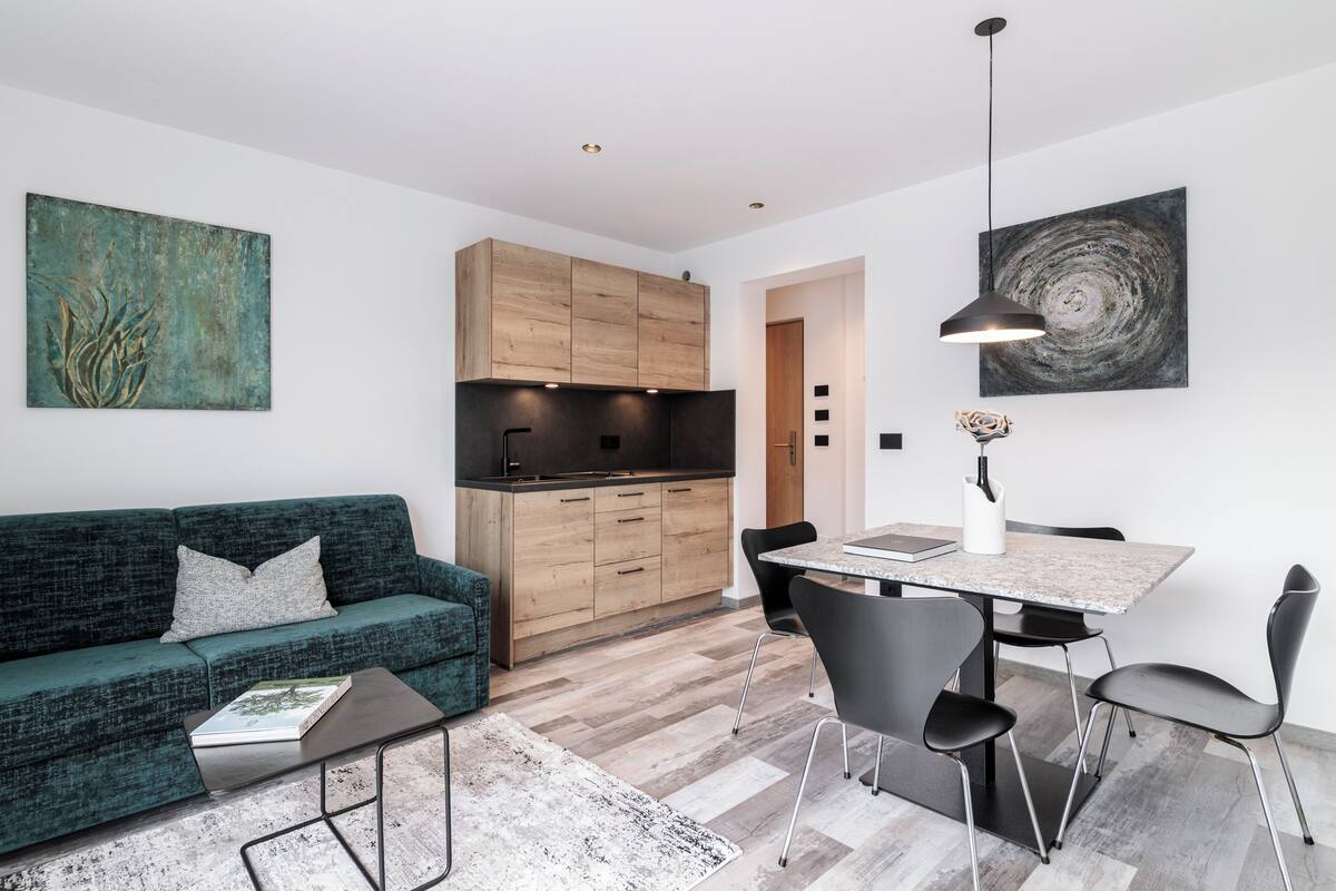 Un espacio habitable moderno con sofá, mesa de centro, mesa de comedor, sillas, zona de cocina y obras de arte en las paredes.