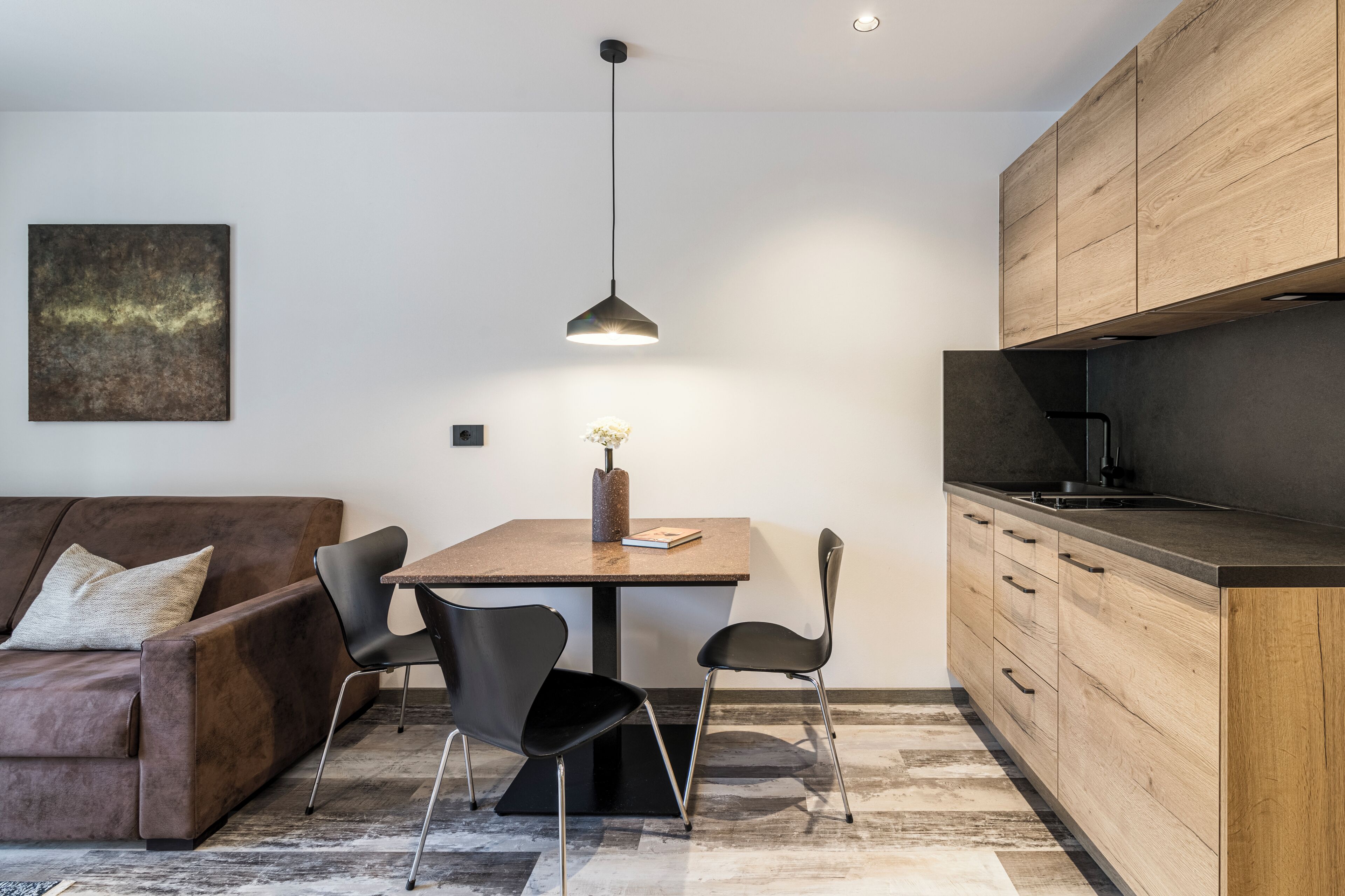 A modern kitchen with a dining table, chairs, a hanging light, and wooden cabinets.
