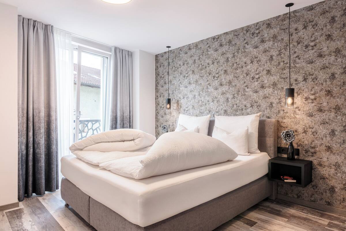 Un dormitorio moderno con cama, cortinas, una mesita de noche y una pared con textura.