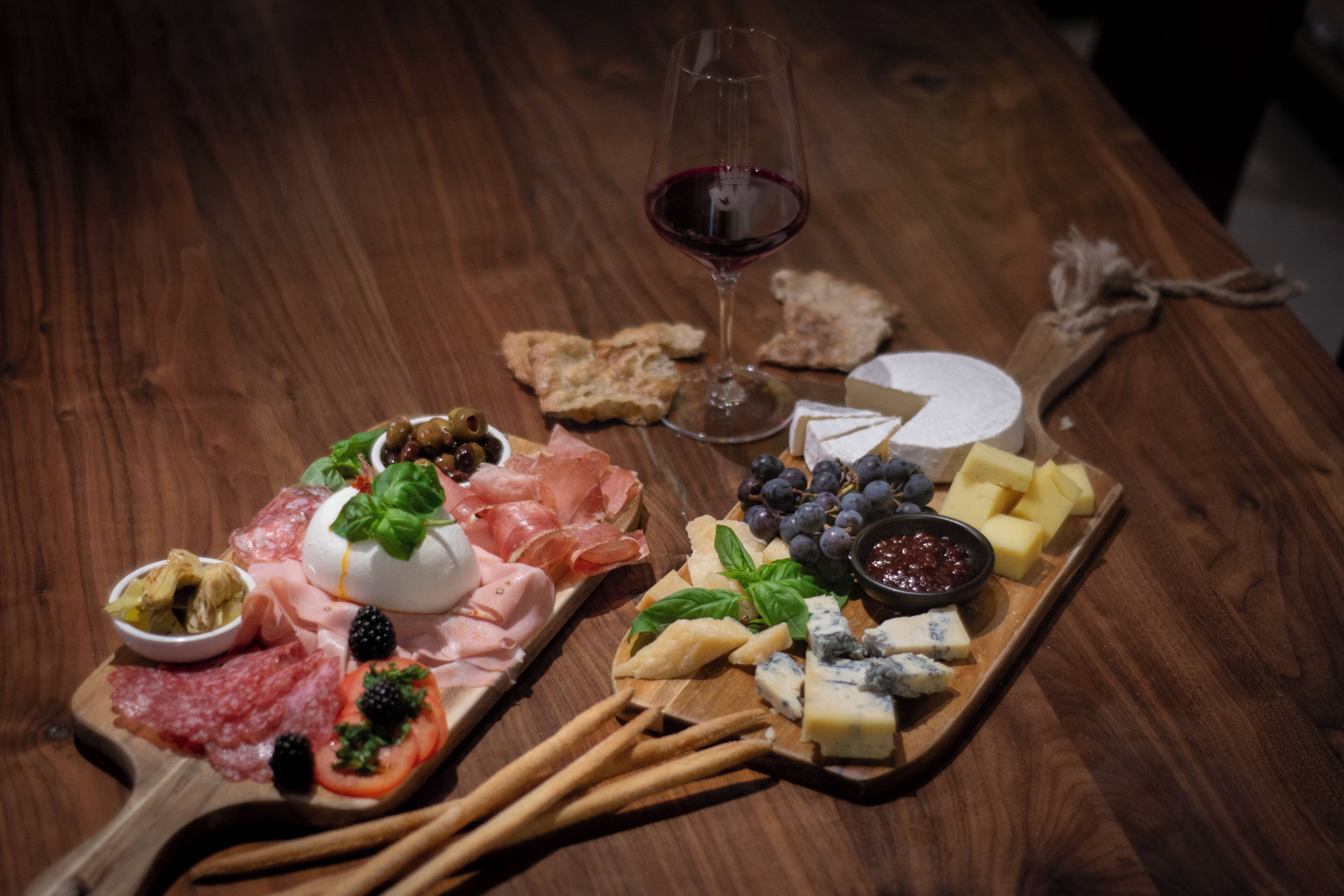 Une table en bois sur laquelle on a disposé une planche de charcuterie, du fromage, des raisins et un verre de vin rouge.
