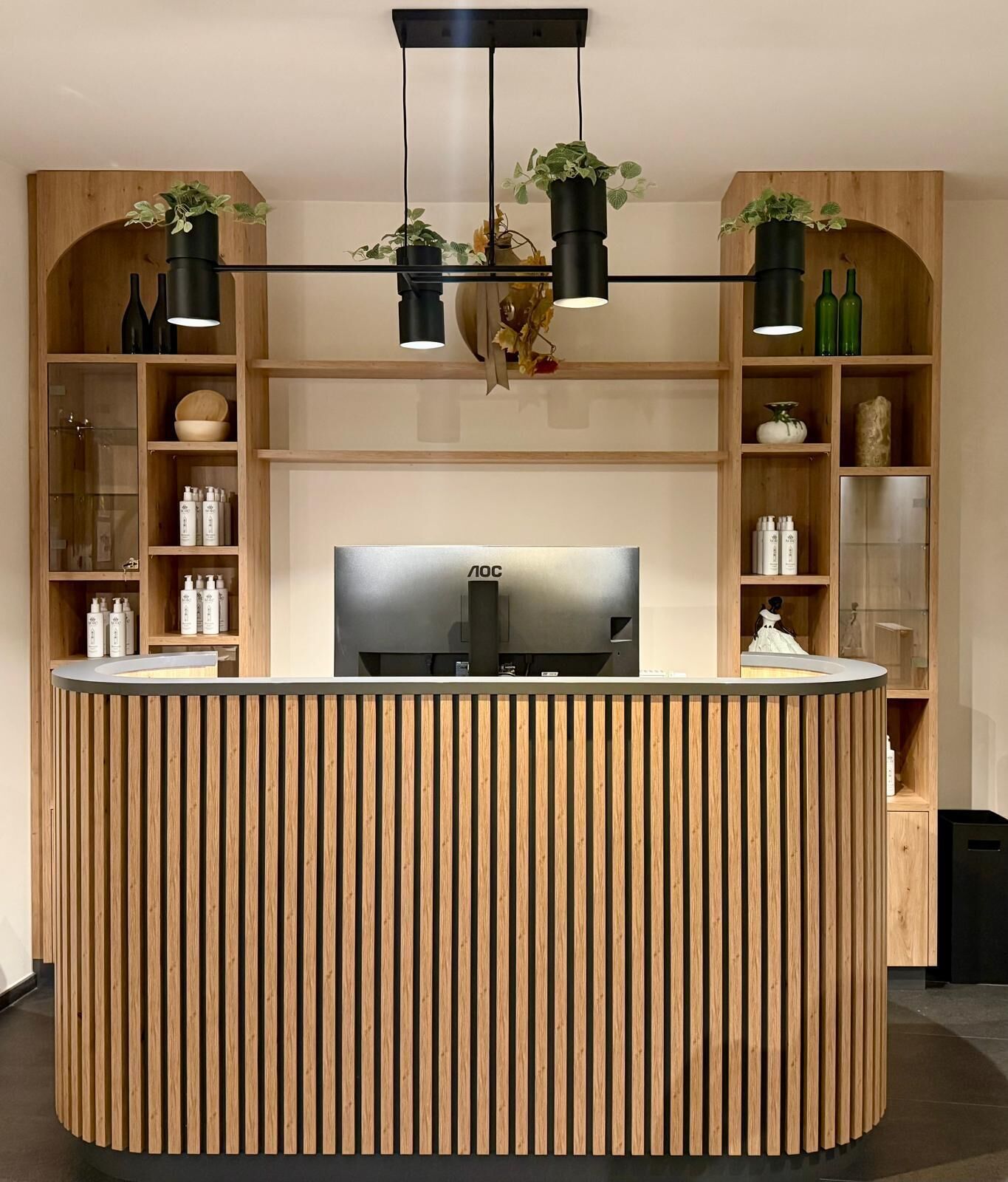 Ein Empfangsschalter mit Holzlamellen-Design, einem Flachbildfernseher und Regalen mit Flaschen und Dekoration.