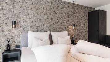 A bedroom with a bed, white pillows, a nightstand, a dresser, and a wall with a textured pattern.