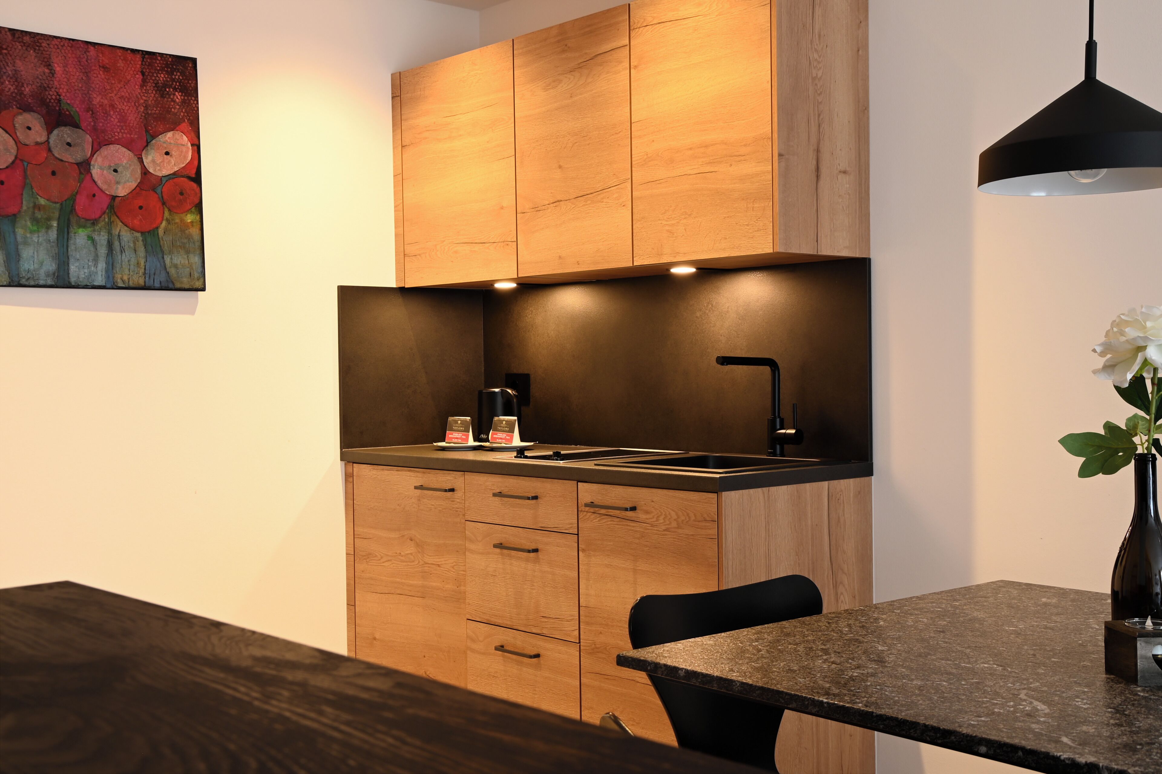 A modern kitchen with wooden cabinets, a black countertop, and a single chair.