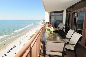 A balcony with a table and chairs overlooking a beach. - Indulge in Oceanfront Luxury at Our 5-Bedroom Condo in the Indigo Tower (North Myrtle Beach)