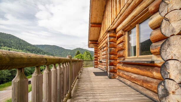 En træhytte med balkon, hvorfra der er udsigt over en skovdal.