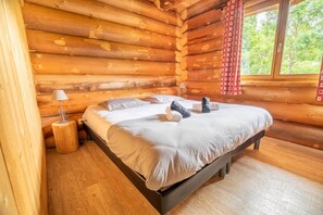 A log cabin bedroom with a bed, a lamp, and a window with curtains. - Log cabin, close to the slopes, 8p (La Bresse)