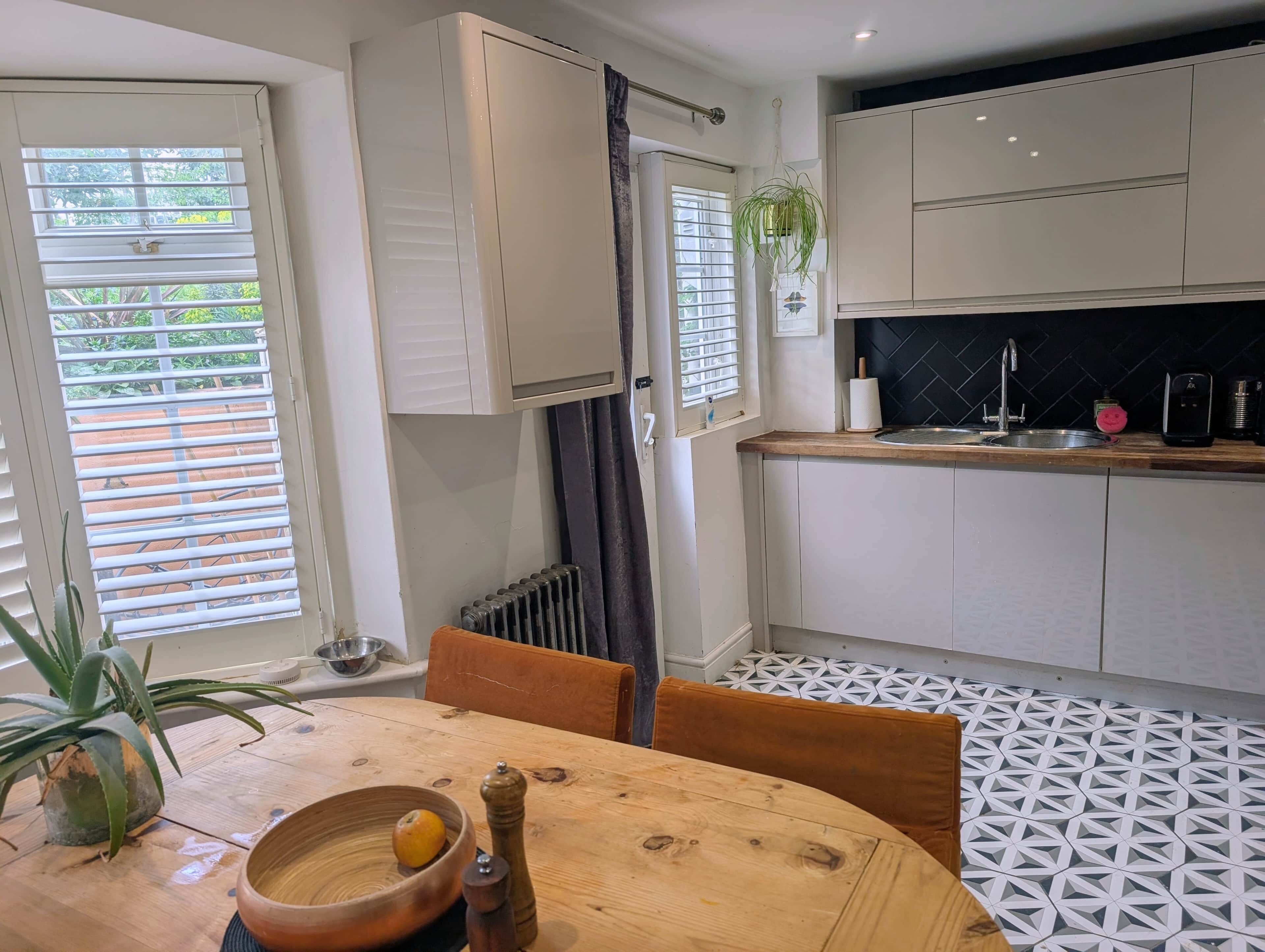 A modern kitchen with white cabinets, a wooden table, and a patterned floor.