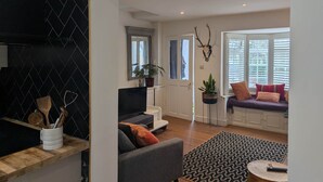 A living room with a sofa, a coffee table, and a TV. There is a door leading to another room, a window with blinds, and a wall-mounted plant. - Central Cute Garden Cottage Close to Town & Beach (Brighton and Hove)