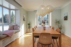 A dining area with a wooden table, wicker chairs, a bench with cushions, and a large window with a view of trees.