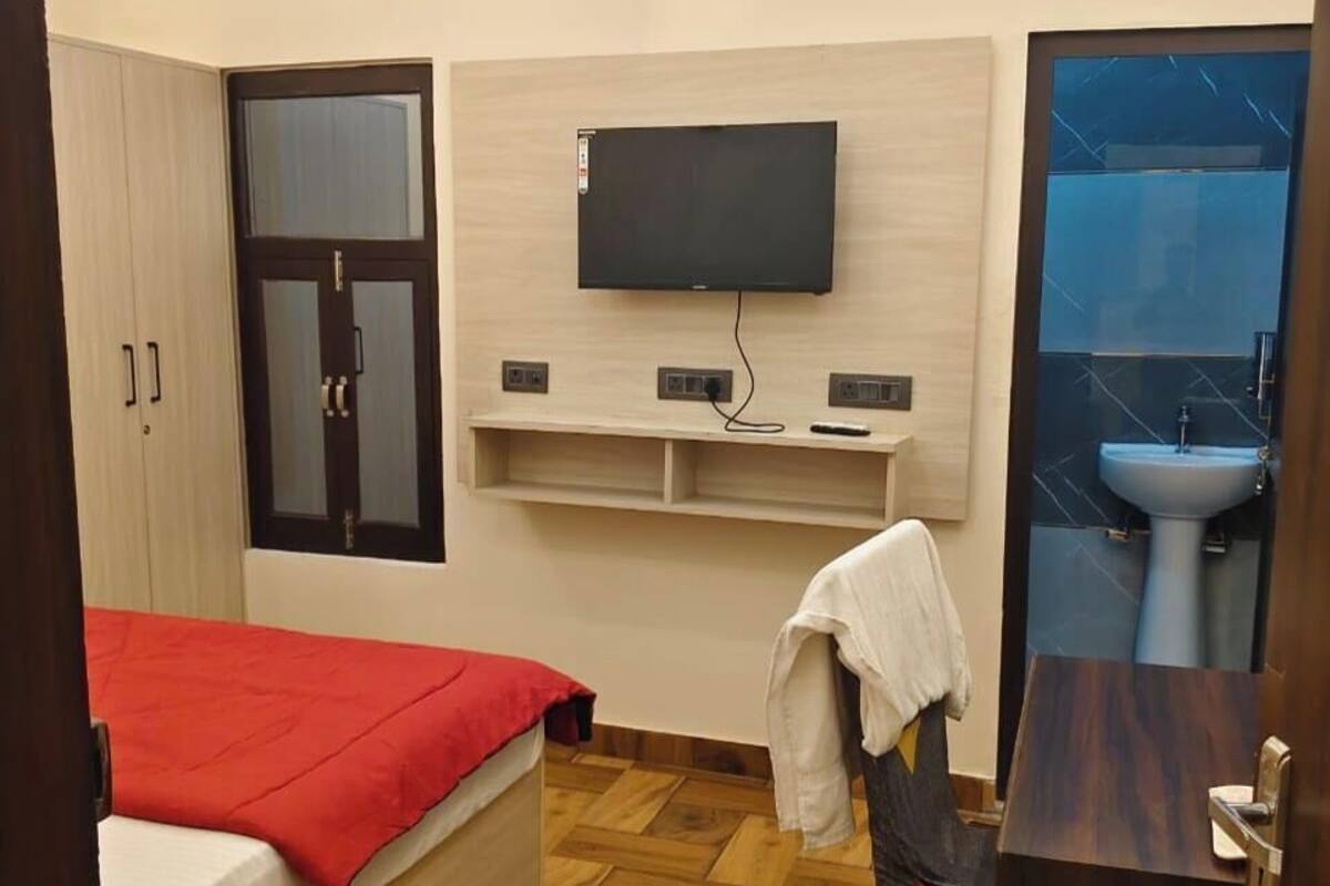 Une chambre avec un lit, une télévision, un climatiseur, une armoire et une salle de bain avec un lavabo.