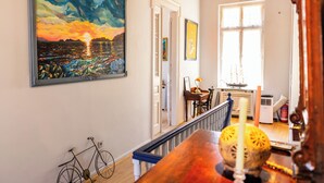 A hallway with a painting of a sunset, a bicycle, and a table with a candle. - LOS 2 (Symi)