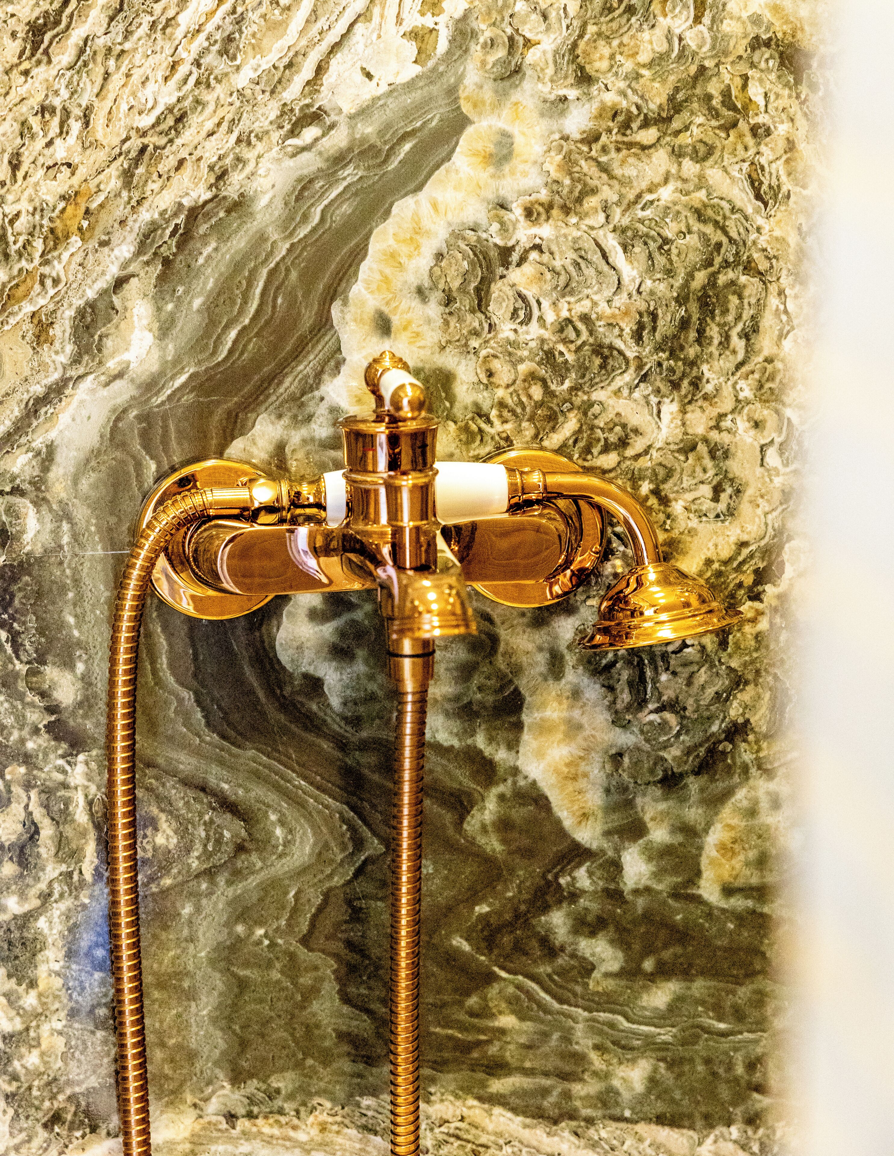 Uma casa de banho com parede de mármore, um chuveiro dourado e um ralo visível.
