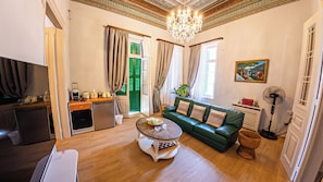 Una sala de estar con sofá verde, una mesa de centro, televisión y una pequeña cocina, además de una araña.