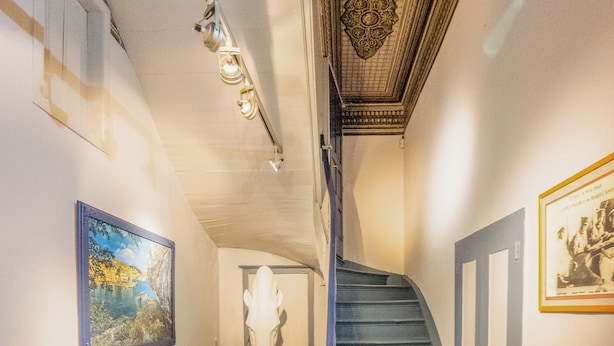 A hallway with a staircase, a white sofa, and a painting on the wall. - LOS 2 (Symi)