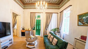 A living room with a television, a green sofa, a chandelier, and a painting on the wall. - LOS 2 (Symi)