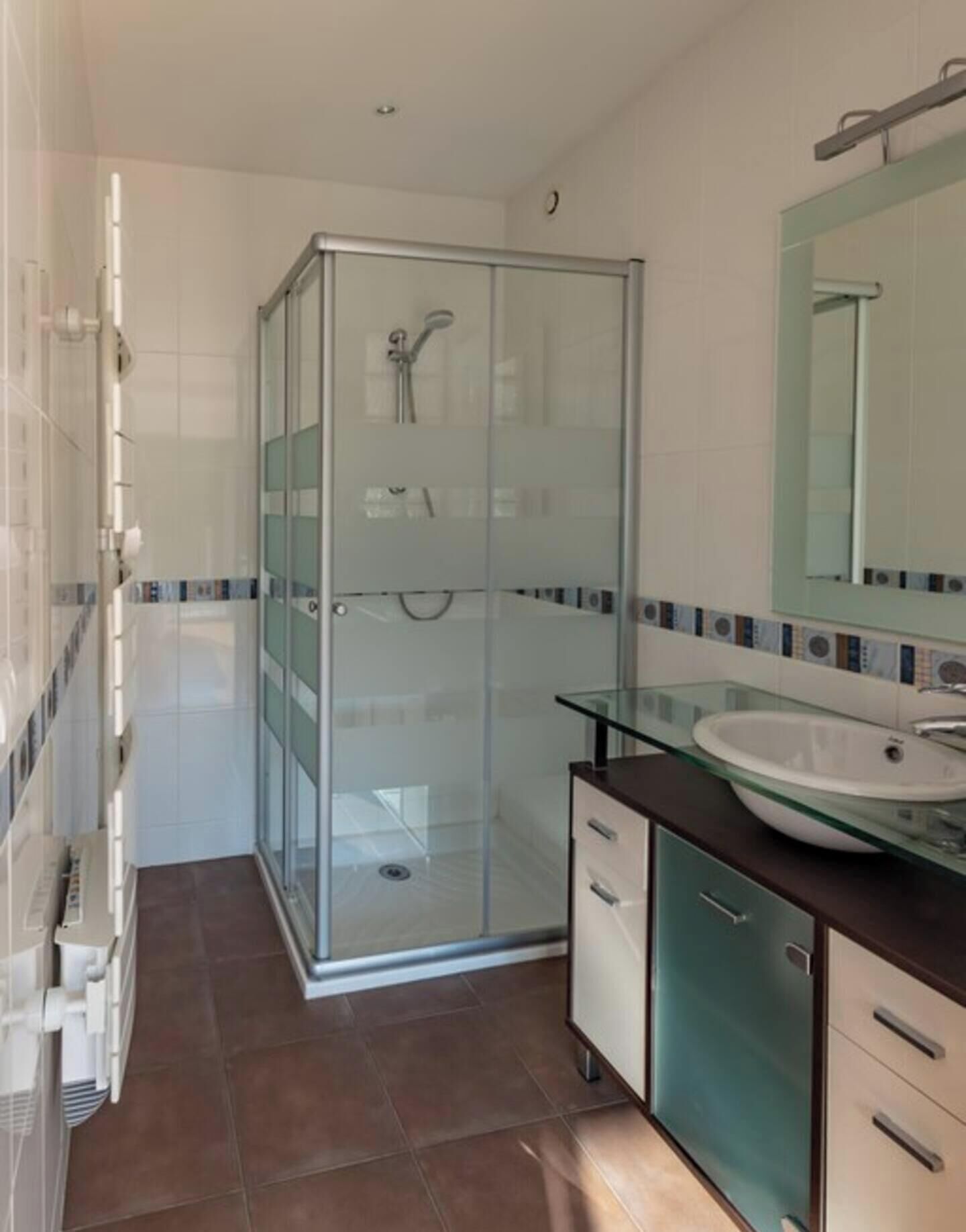 Uma casa de banho moderna com cabine de duche em vidro, lavatório com bancada de vidro e espelho sobre o lavatório.