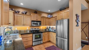 Una cocina con armarios de madera, electrodomésticos de acero inoxidable, microondas, estufa y refrigerador.